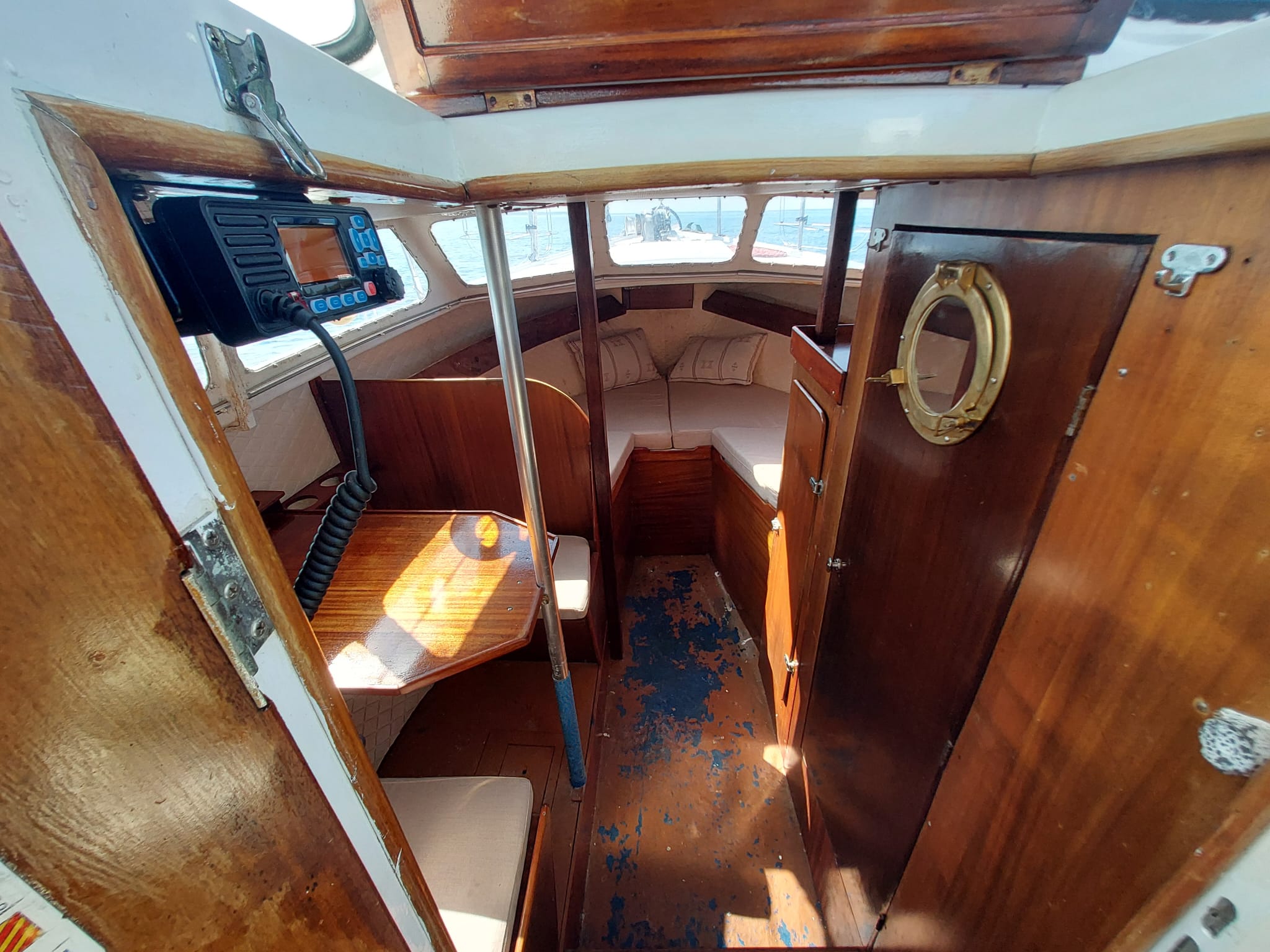 Below deck on STRIGA: VHF radio, dining table, and the toilet door with its brass porthole