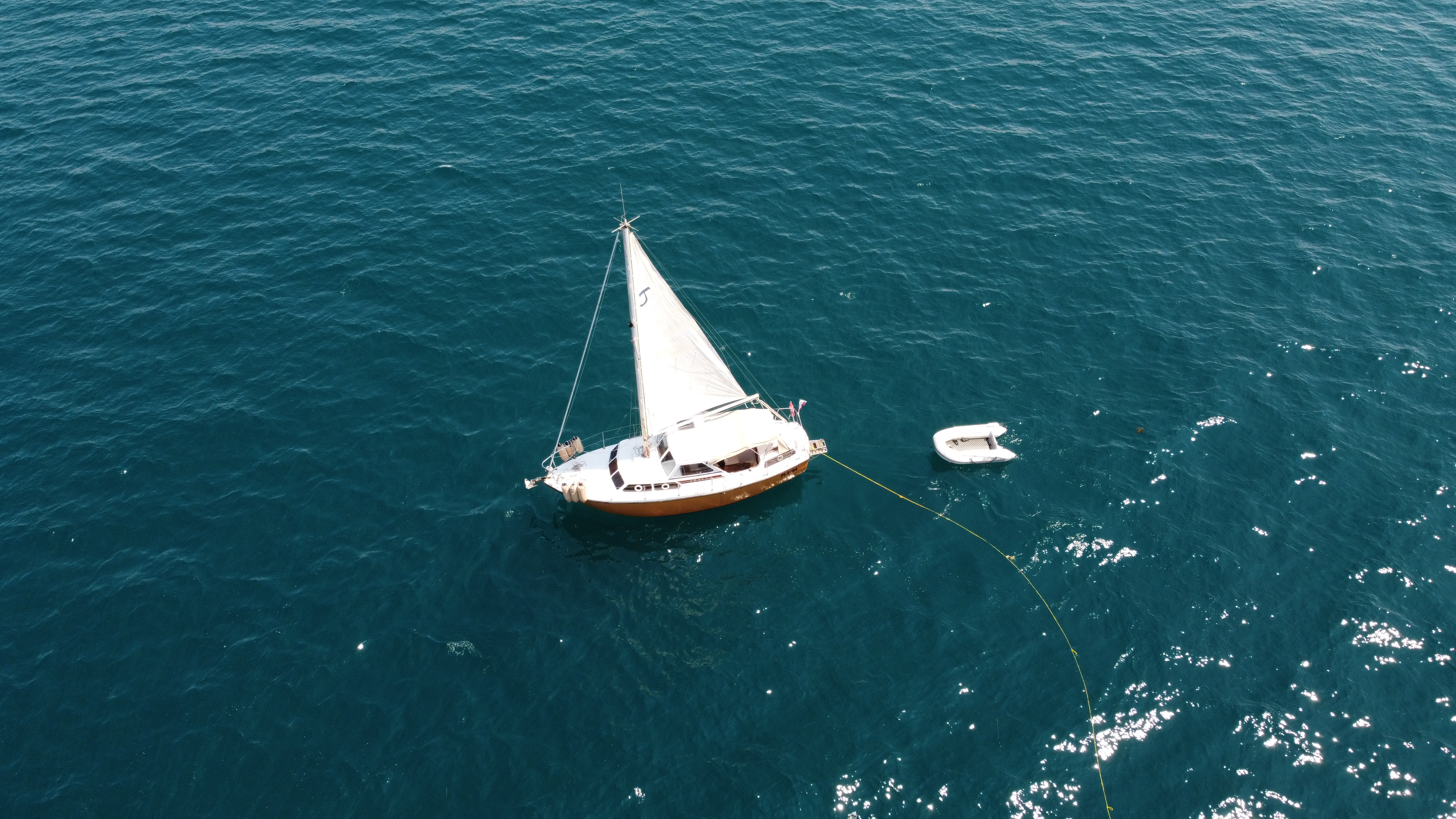 Aerial drone view of STRIGA alone at anchor on open, calm blue water, with her tender floating nearby