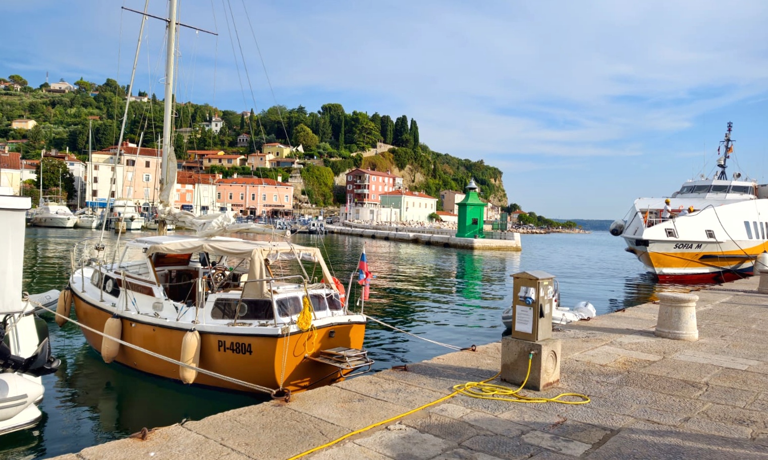 STRIGA moored in Piran harbour, with the old town and hillside houses behind her
