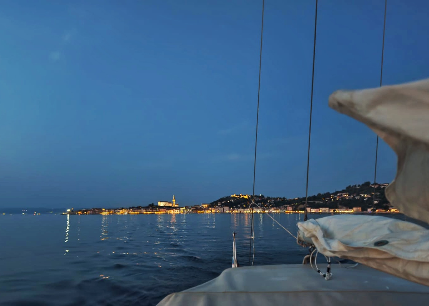 Piran's illuminated skyline seen from STRIGA's deck at dusk, on a sunset trip