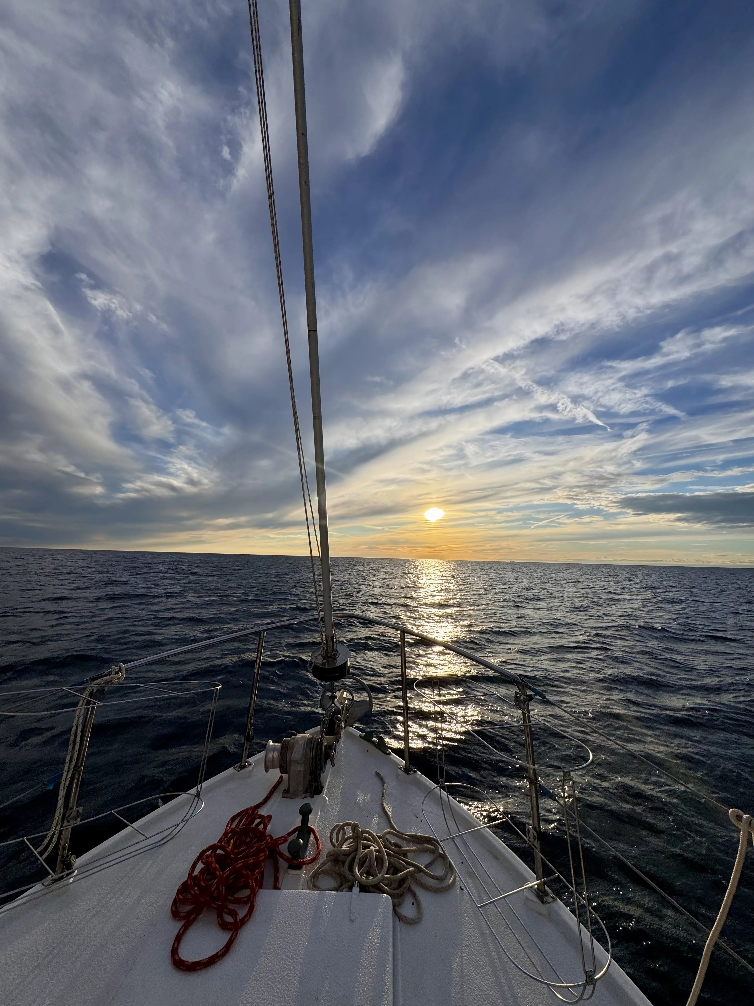 STRIGA's bow with coiled ropes, sailing into a wide sunset sky